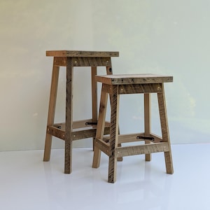 May include: Two wooden stools made from reclaimed wood with a rustic finish. The stools are different sizes and have a simple, minimalist design.
