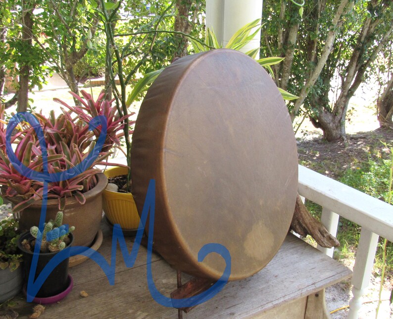 May include: A round, hand-held drum with a smooth, tan-colored animal hide head stretched over a circular wooden frame. The drum surface displays natural variations in color and texture, featuring a consistent, taut, and circular design.