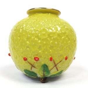 May include: A spherical yellow ceramic vase with a textured surface featuring embossed floral patterns. The base is decorated with painted green leaves and brown stems topped with small red berries. The rim has a metallic gold finish.