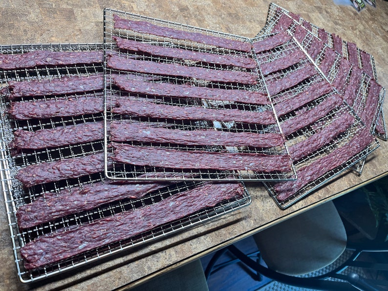May include: Multiple metal drying racks with strips of dried beef jerky on them.