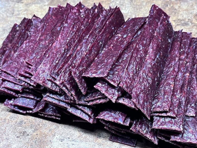 May include: A stack of purple beef jerky strips. The jerky is arranged in a pile, with the strips overlapping each other.