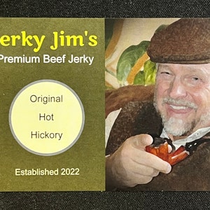 May include: A business card for Jerky Jim's Premium Beef Jerky. The card is green with yellow text. It features a circle with the words "Original", "Hot", and "Hickory" inside. The card also says "Established 2022". A man with a brown hat and beard is pictured on the right side of the card.
