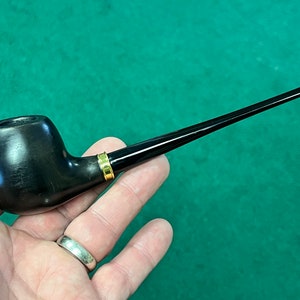 May include: A black wooden pipe with a gold band. The pipe has a round bowl and a long, thin stem.