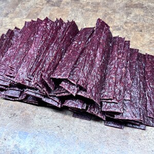 May include: A large stack of thin, dark purple beef jerky strips.