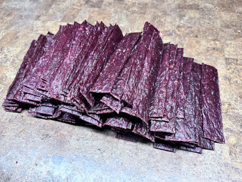 May include: A large stack of thin, dark purple beef jerky strips.