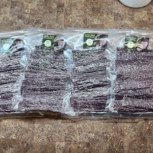 May include: Four clear plastic bags filled with dried meat jerky. Each bag has a label with the text "Jerky Jim's" and a picture of a man.