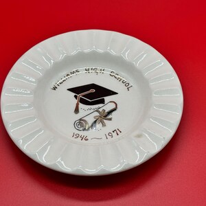 May include: White ceramic ashtray with a ruffled edge, featuring the text "Williams High School" and a graduation cap and diploma design. The years 1946-1971 are also printed on the ashtray. The ashtray is set against a red background.