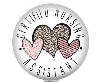 May include: White retractable badge holder with a round, white button featuring the text "CERTIFIED NURSING ASSISTANT" and three pink and brown hearts.