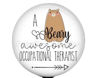 May include: A white round badge holder with a black retractable cord and a clear plastic clip. The badge features a cartoon brown bear with a heart and the text "A Beary Awesome Occupational Therapist".