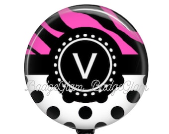 May include: Black and white polka dot and zebra print badge reel with a black circle and the letter "V" in white. The reel has a black retractable cord and a clear plastic clip.