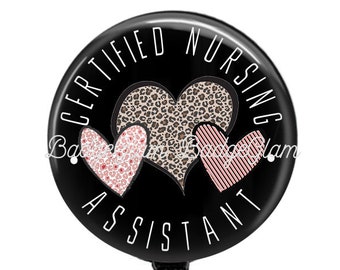 May include: Black and white badge reel with a black circle featuring the text "CERTIFIED NURSING ASSISTANT" in white lettering and two pink and black hearts.