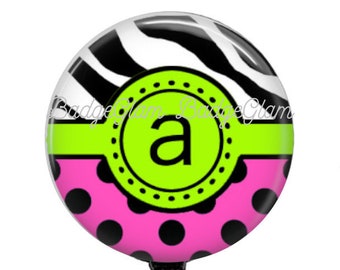 May include: A black, white, and pink zebra print badge reel with a green circle and the letter "a" in the center. The badge reel has a black retractable cord and a clear plastic clip.