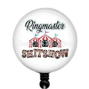 May include: White round badge holder with a black retractable cord and a clear plastic clip. The badge features a red and white striped tent with a blue and white flag. The text "Ringmaster SHITSNOW" is printed on the badge.