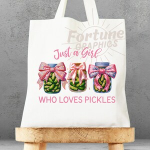 Op de afbeelding: Witte tote bag met een roze en groen ontwerp. De tas heeft de tekst "Fortune Graphics" en "Just a Girl Who Loves Pickles". Drie potten met augurken met roze strikken zijn afgebeeld.