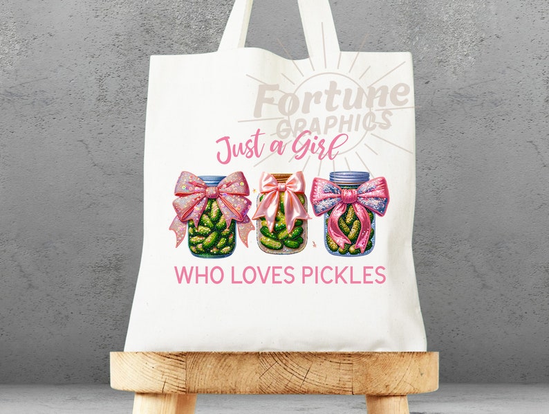 Op de afbeelding: Witte tote bag met een roze en groen ontwerp. De tas heeft de tekst "Fortune Graphics" en "Just a Girl Who Loves Pickles". Drie potten met augurken met roze strikken zijn afgebeeld.