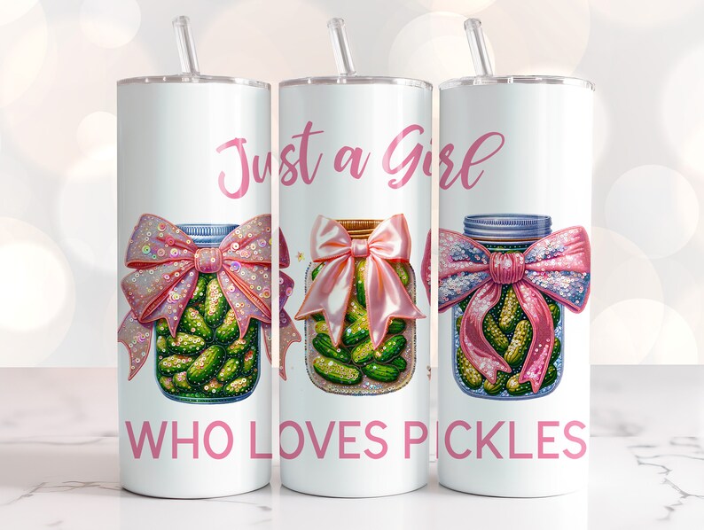 Op de afbeelding: Drie witte bekers met roze deksels en rietjes. Elke beker heeft een roze strik en een glazen pot gevuld met augurken. De tekst "Just a Girl Who Loves Pickles" staat op de bekers gedrukt.