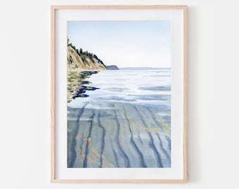 May include: Watercolor print of a coastal landscape. The artwork depicts a shoreline with a cliff covered in green foliage, a calm sea, and a sandy seabed with colorful streaks. The print is framed in a light wood frame.