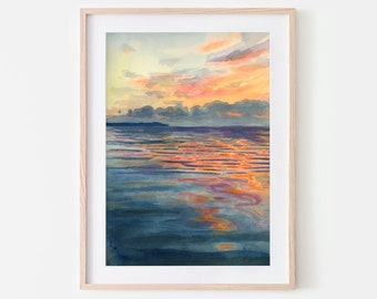 May include: A watercolor painting of a sunset over a calm body of water. The sky is a mix of orange, pink, and purple, and the water reflects the colors of the sky. The painting is framed in a light wood frame.