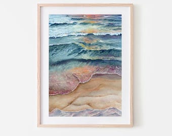 May include: A watercolor painting of ocean waves crashing on a sandy beach. The water is a mix of blue, green, and purple, and the sand is a warm beige. The painting is framed in a light wood frame.
