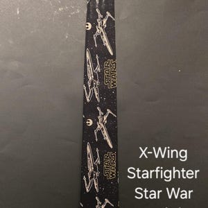 Puede incluir: Corbata negra con un patr&oacute;n repetido de cazas X-Wing de Star Wars. El texto "STAR WARS" est&aacute; impreso en amarillo en la corbata.