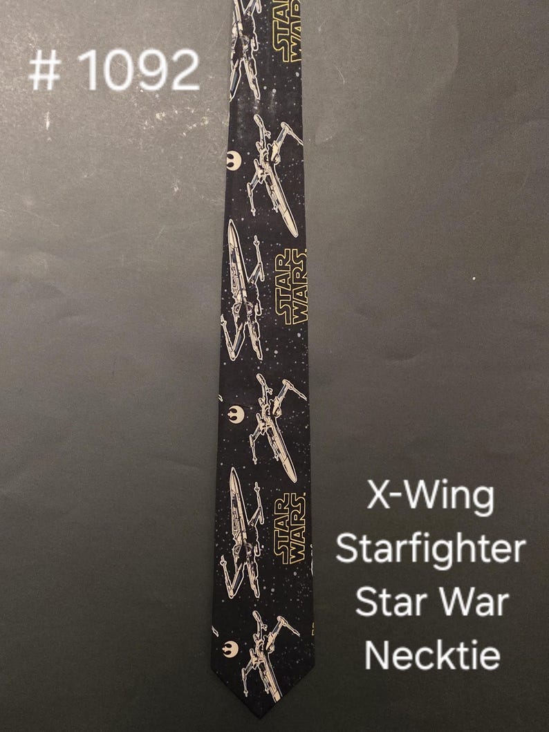 Puede incluir: Corbata negra con un patr&oacute;n repetido de cazas X-Wing de Star Wars. El texto "STAR WARS" est&aacute; impreso en amarillo en la corbata.