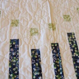 Pode incluir: Um edredom branco com um padr&atilde;o floral. O edredom &eacute; feito de tiras verticais de tecido em tons de azul, verde e branco. O edredom &eacute; acolchoado com um padr&atilde;o de pontos simples.