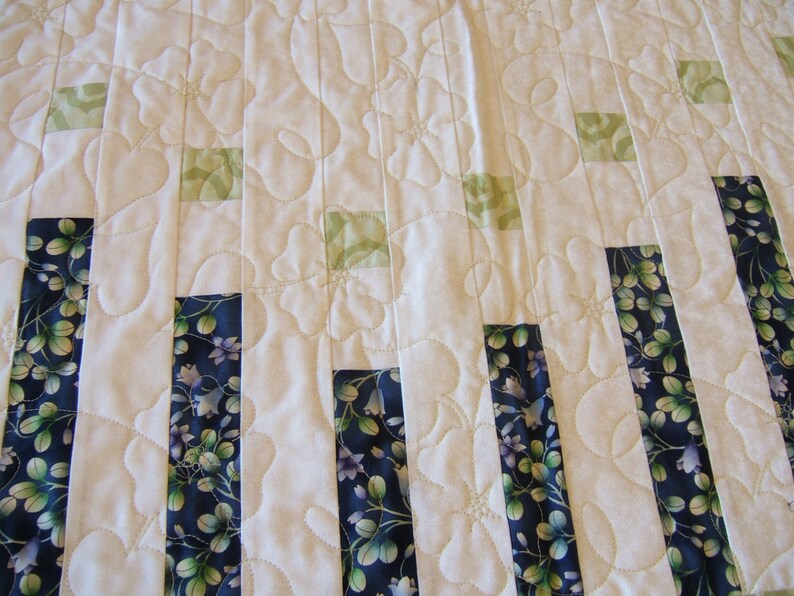 Pode incluir: Um edredom branco com um padr&atilde;o floral. O edredom &eacute; feito de tiras verticais de tecido em tons de azul, verde e branco. O edredom &eacute; acolchoado com um padr&atilde;o de pontos simples.