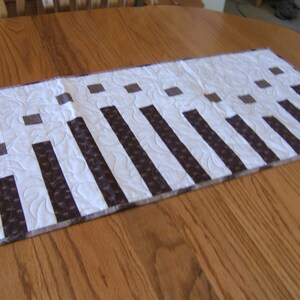 May include: A white table runner with brown stripes and squares. The runner is on a wooden table.