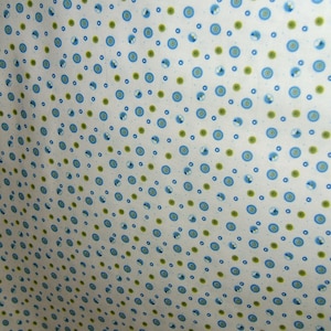 May include: White fabric with a repeating pattern of blue and green circles. The circles are arranged in a diagonal pattern.