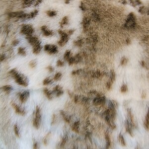May include: Close-up of a white and brown faux fur fabric with a spotted pattern.