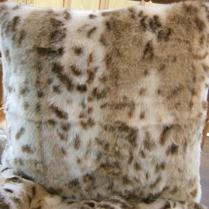 May include: A soft, plush throw pillow with a faux fur design in shades of brown and white. The pillow has a spotted pattern reminiscent of a snow leopard.