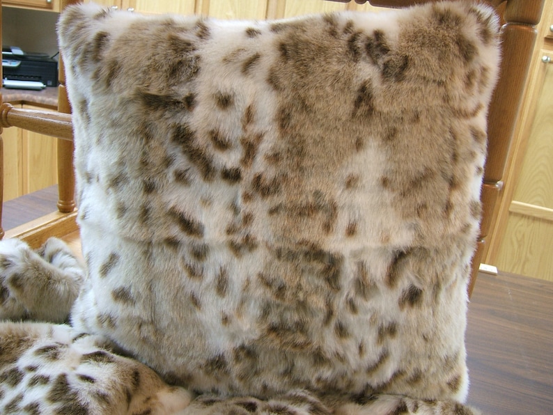 May include: A soft, plush throw pillow with a faux fur design in shades of brown and white. The pillow has a spotted pattern reminiscent of a snow leopard.