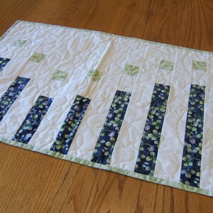 Pode incluir: Um corredor de mesa branco com uma borda verde e faixas de tecido floral azul e verde. O corredor &eacute; acolchoado com um padr&atilde;o ondulado.
