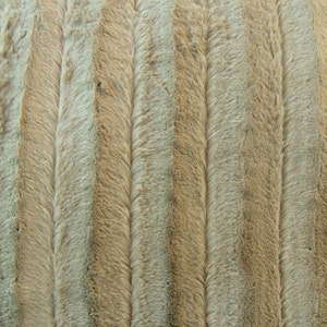 May include: Close-up of a beige and brown faux fur fabric with a vertical striped pattern.