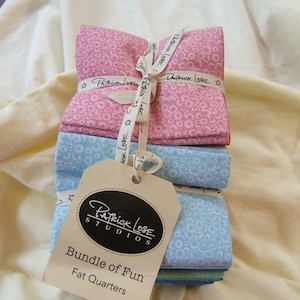 May include: A bundle of fabric fat quarters in pink and blue with a white polka dot pattern. The fabric is tied with a white ribbon and a tag that reads "Patrick Lose Studios Bundle of Fun Fat Quarters".