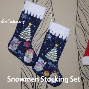 Op de afbeelding: Een set van twee blauwe kerstsokken met witte boorden. Elke sok is geborduurd met sneeuwpoppen, een kerstboom en sneeuwvlokken. De sokken hangen aan een zwart metalen rek.