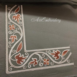 May include: A corner design embroidered on a gray fabric with white and brown thread. The design features a floral pattern with leaves and flowers.