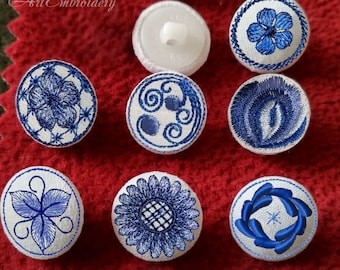 May include: Eight white fabric buttons with blue embroidery designs. The designs include a flower, a swirl, a leaf, a sunflower, and a wreath.