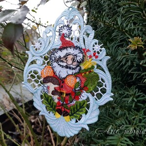 May include: A white, blue, and green embroidered Christmas ornament featuring a Santa Claus holding a mushroom and holly. The ornament is in a delicate, lacy design.