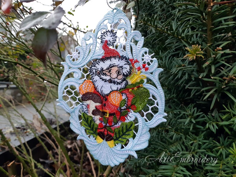 May include: A white, blue, and green embroidered Christmas ornament featuring a Santa Claus holding a mushroom and holly. The ornament is in a delicate, lacy design.