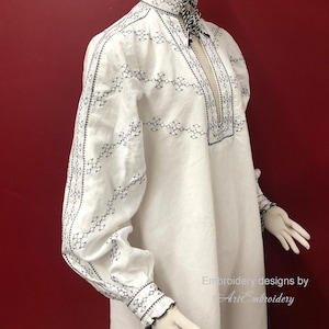 May include: White linen shirt with black embroidery. The shirt has a high collar and long sleeves. The embroidery is in a geometric pattern. The shirt is on a mannequin against a red background. Embroidery designs by ArtEmbroidery.