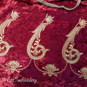 Puede incluir: Tres diseños de paisley bordados en oro sobre una tela de terciopelo rojo oscuro. Los diseños de paisley están conectados por una cadena dorada con tres motivos de calavera y huesos cruzados dorados.