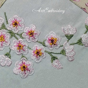 May include: Embroidered design of a branch of pink flowers with green leaves on a light blue fabric background. The text "Art Embroidery" is visible in the top center of the image.