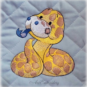 May include: Embroidered design of a yellow snake with brown spots, holding a blue and white object in its mouth. The snake has a stitched-on patch on its face. The design is on a light blue quilted fabric. Art Embroidery.