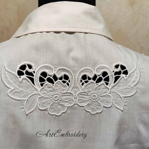 May include: White cotton shirt with a delicate floral embroidery design on the back. The embroidery features two flowers with intricate details and leaves, creating a cutout effect.