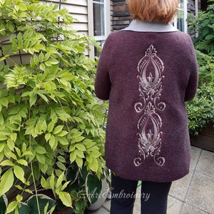 May include: A burgundy cardigan with a silver embroidered design on the back. The design features a repeating pattern of swirls and leaves.