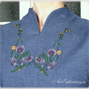 Peut inclure: Un pull bleu avec un motif floral brodé composé de fleurs violettes, orange et vertes. Le motif est centré sur l'encolure du pull.