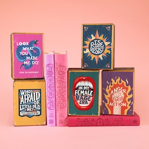 Puede incluir: Un conjunto de seis bloques de madera con ilustraciones y texto coloridos. Los bloques presentan frases como "Mira lo que me has hecho hacer", "¿Quién le tiene miedo a la vieja yo?", "Levántate y resiste", "En mi era de furia femenina", y "La ira alimenta la acción".