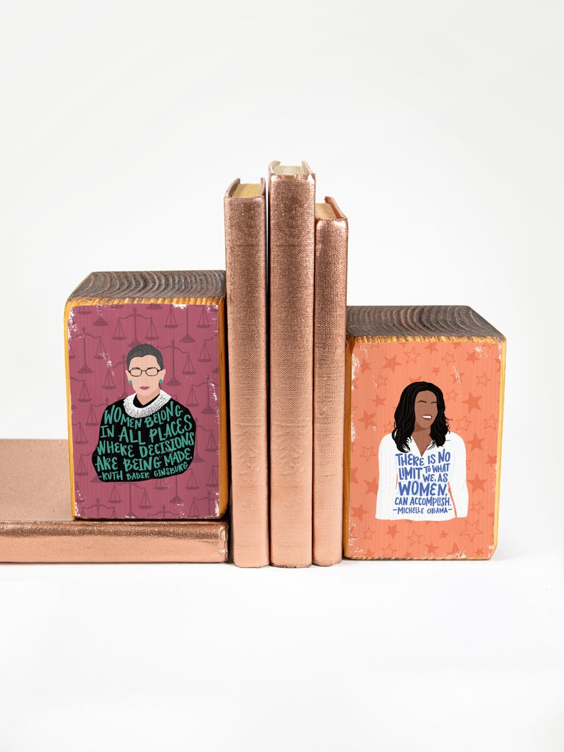 Bookend set propping up copper metallic books. Left bookend is a graphic of RBG and the right one is of Michelle Obama.
