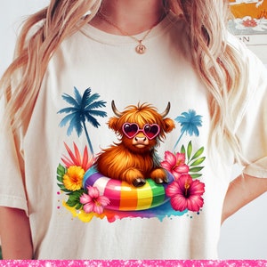 May include: A white t-shirt with a colorful graphic of a Highland cow wearing sunglasses and floating on a rainbow inflatable ring. Tropical flowers and palm trees surround the cow.